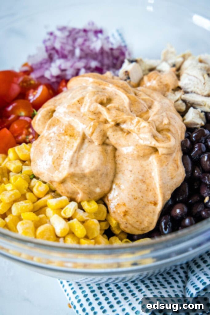 Close up of mayo and taco seasoning dressing in a mixing bowl on top of corn, tomatoes, onions, chicken, and beans
