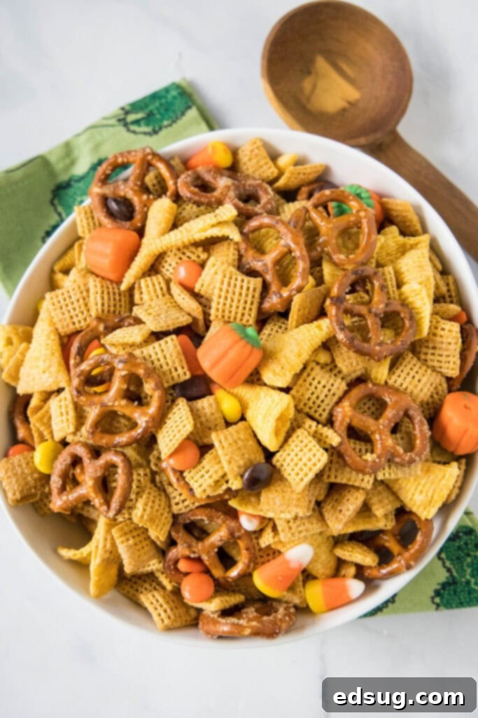 Looking down on a bowl of vibrant Halloween Chex Mix, featuring cereals, pretzels, Bugles, candy corn, and Reese's Pieces.