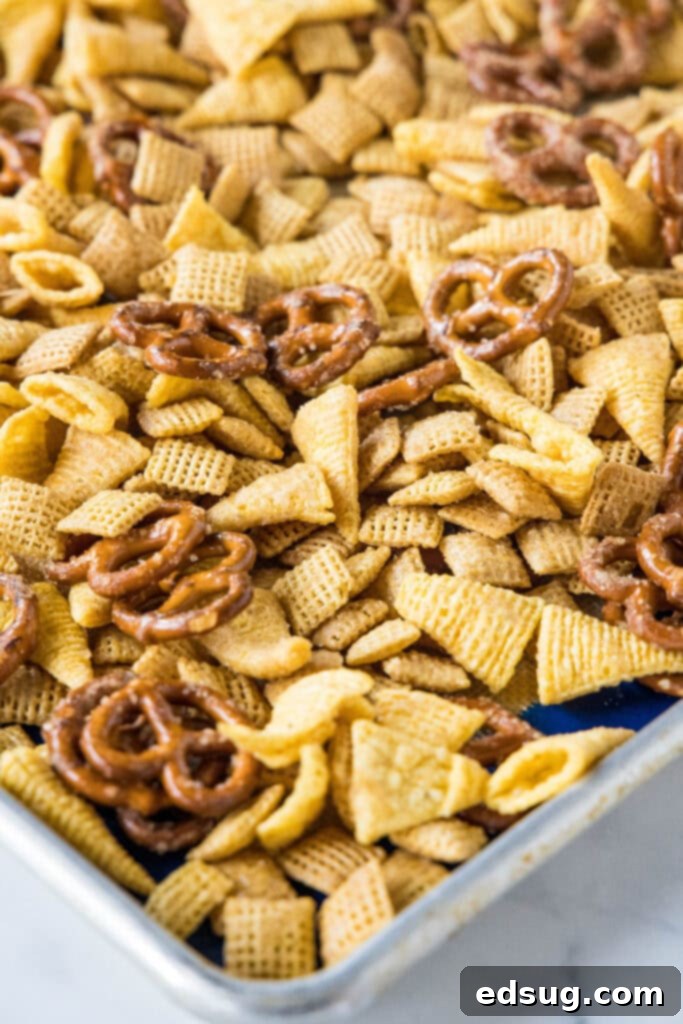 Halloween Chex Mix spread on a baking tray, glistening with the sweet butter coating before baking.