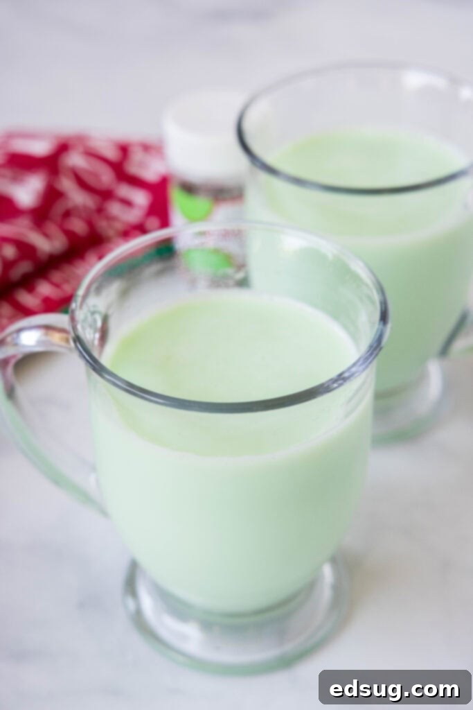 A mug of green white peppermint hot chocolate, topped with whipped cream and sprinkles, perfect for Christmas.