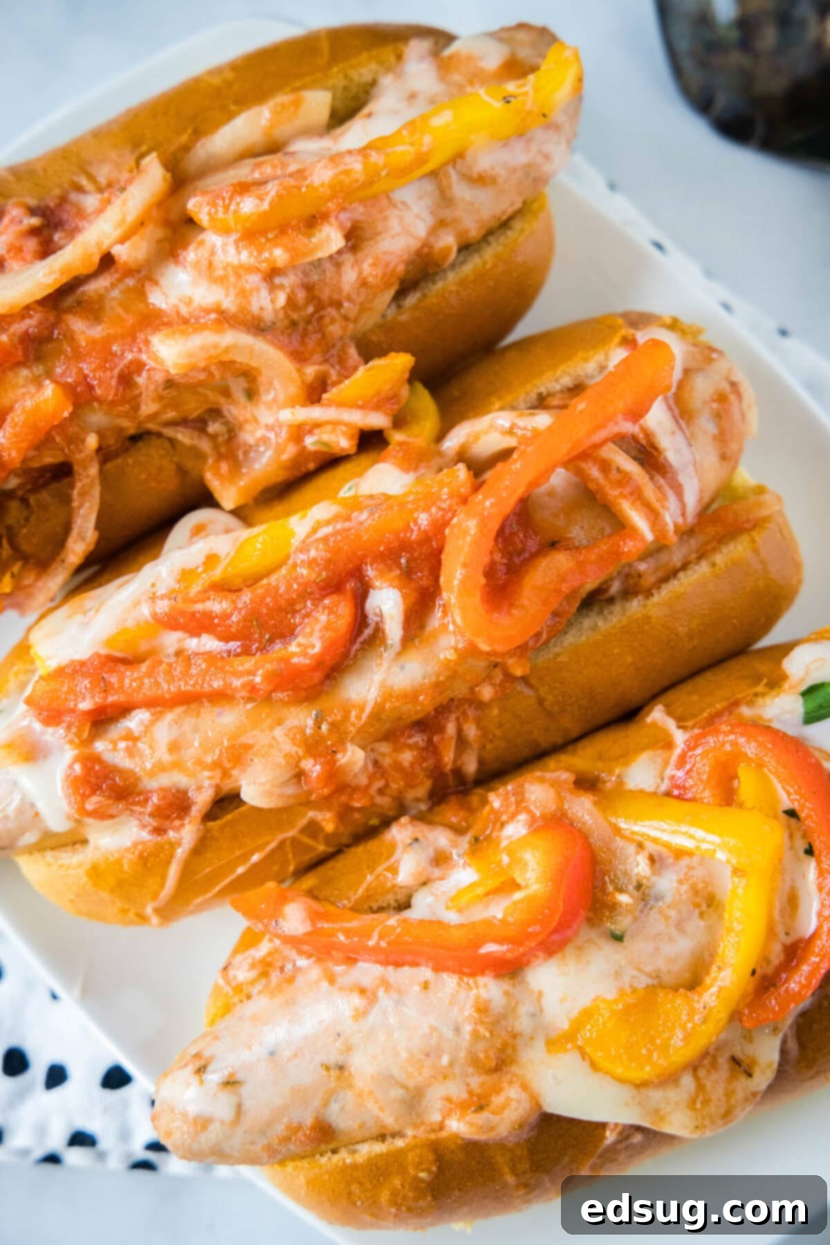 Overhead view of three sausage and peppers sandwiches on a plate