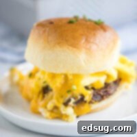 Close up of a breakfast slider on a plate, with melted cheese oozing out, garnished with chives.