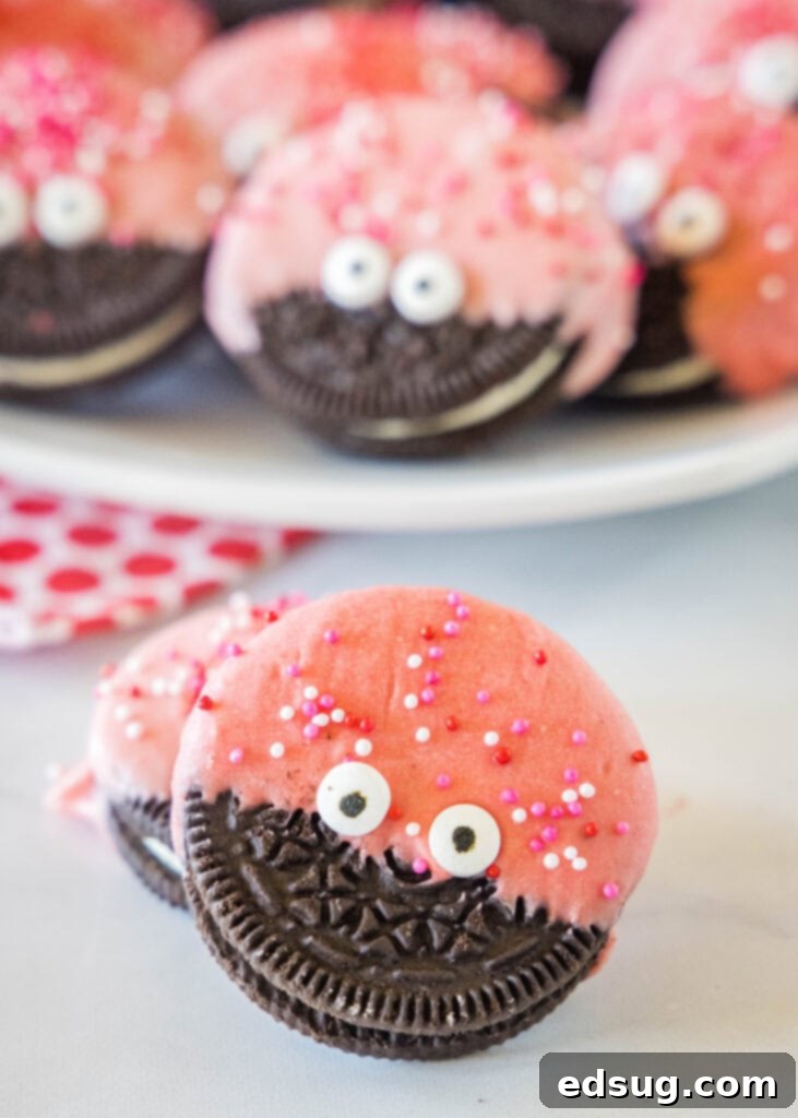 A vibrant tray of freshly made Love Bug Oreo Cookies, beautifully decorated with a rich red chocolate coating, playful candy eyes, and festive Valentine's Day sprinkles.