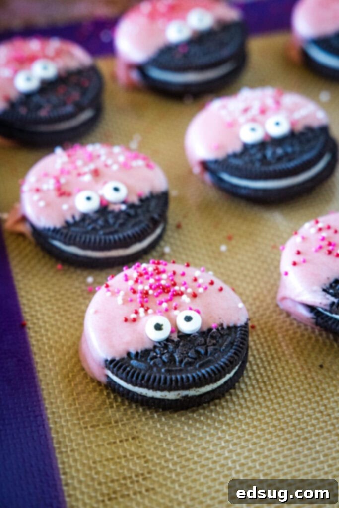 A baking tray lined with parchment paper, holding several Love Bug Oreo Cookies as their red chocolate coating and sprinkles set firm, showing the transition from liquid chocolate to solid deliciousness.
