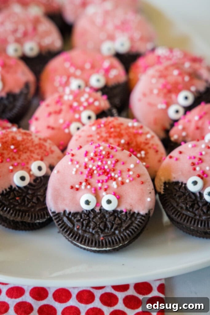 A delightful arrangement of finished Love Bug Oreo Cookies on a white plate, each showcasing its glossy red chocolate, expressive candy eyes, and vibrant sprinkles, ready to be enjoyed for Valentine's Day.