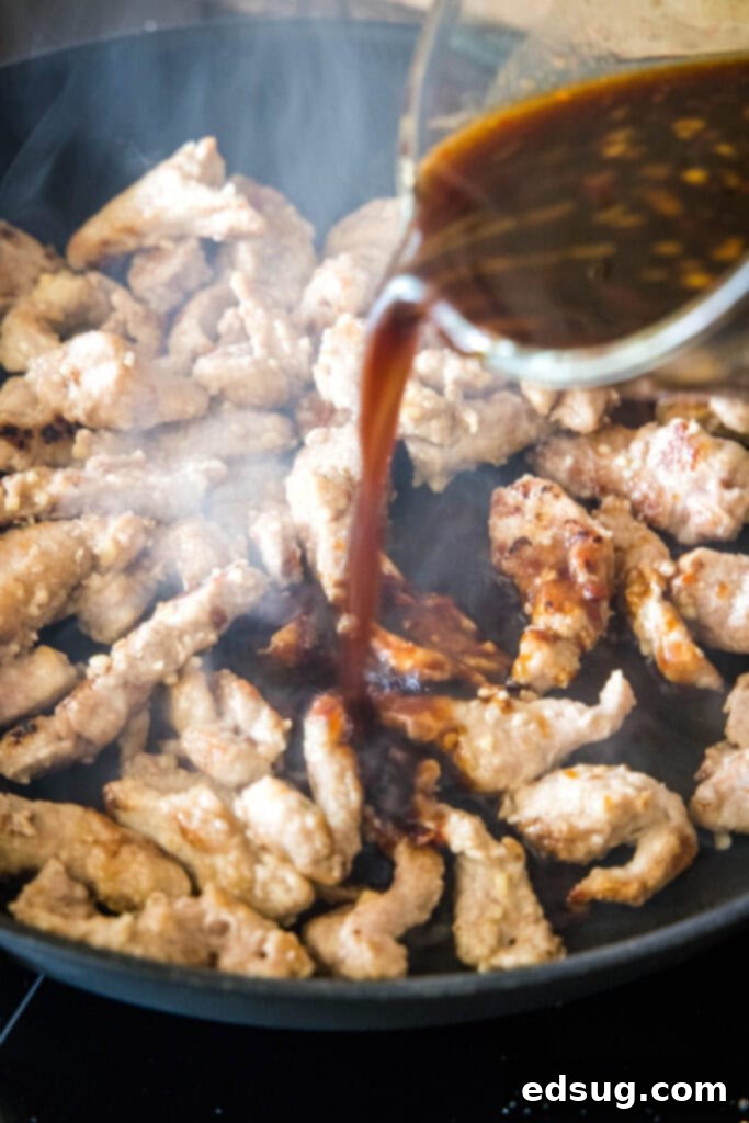 This Mongolian pork is tender, juicy, sweet, sour, a little bit spicy, and so much better than takeout, plus it only takes 20 minutes. A sauce being poured over pork in a skillet.