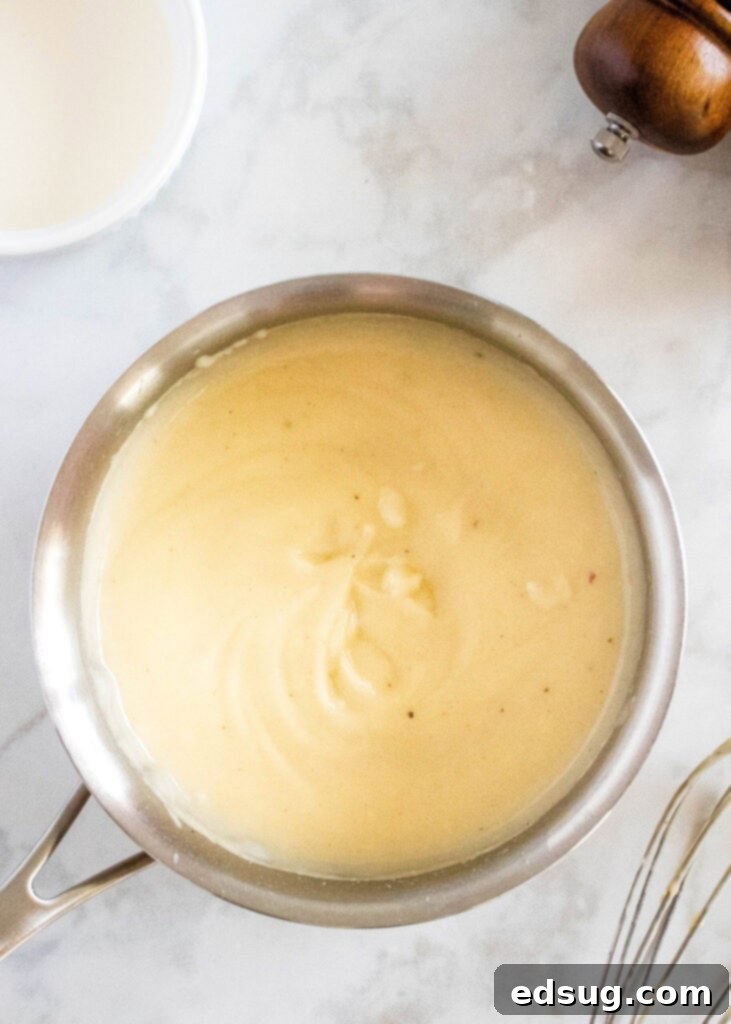 Overhead view of a saucepan showing the smooth mixture of roux and chicken broth after being thoroughly whisked together, now a slightly thicker, pale yellow liquid.