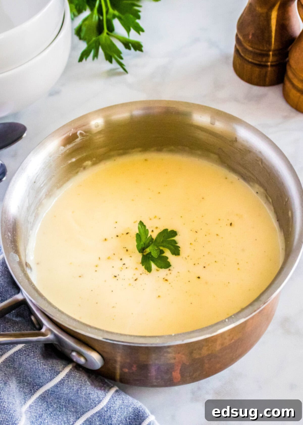 A beautiful saucepan filled with freshly made homemade cream of chicken soup, generously topped with a sprinkle of chopped parsley and a grind of black pepper, ready to serve.