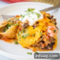 A serving of taco stuffed shells on a white plate next to a fork, highlighting the deliciousness of the cheesy, baked dish.
