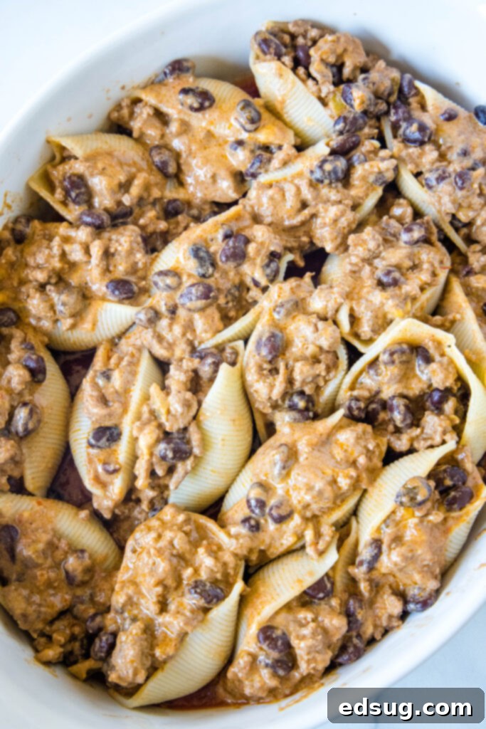 A baking dish filled with meticulously assembled taco stuffed shells, each overflowing with a savory filling, before being covered with additional salsa and cheese.