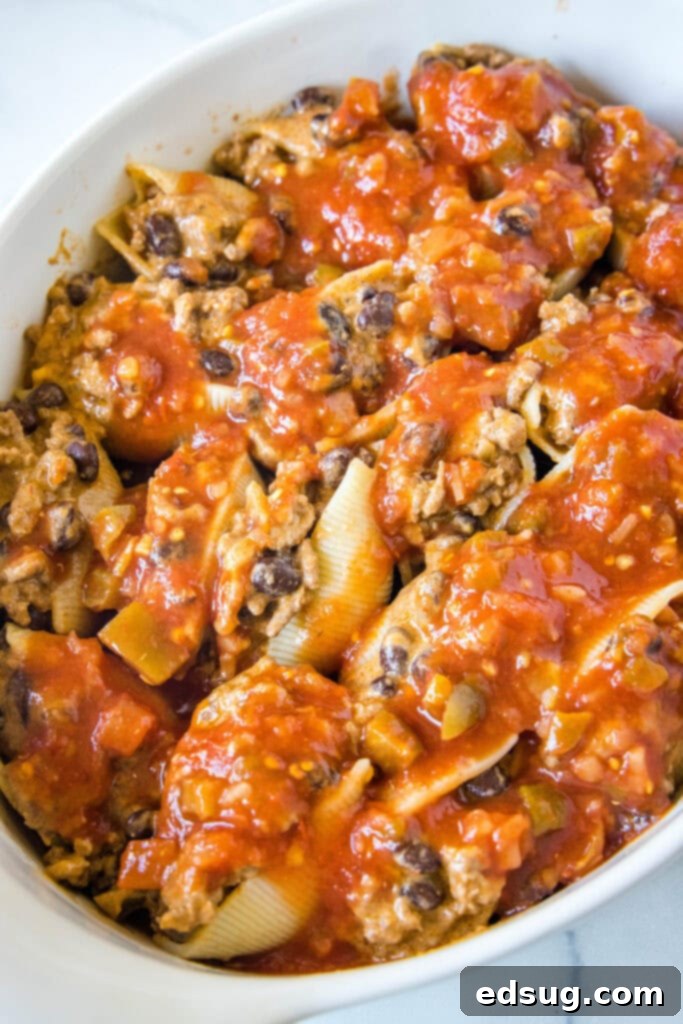 Assembled taco stuffed shells neatly arranged in a baking dish, completely covered with a rich layer of salsa, ready for the oven.