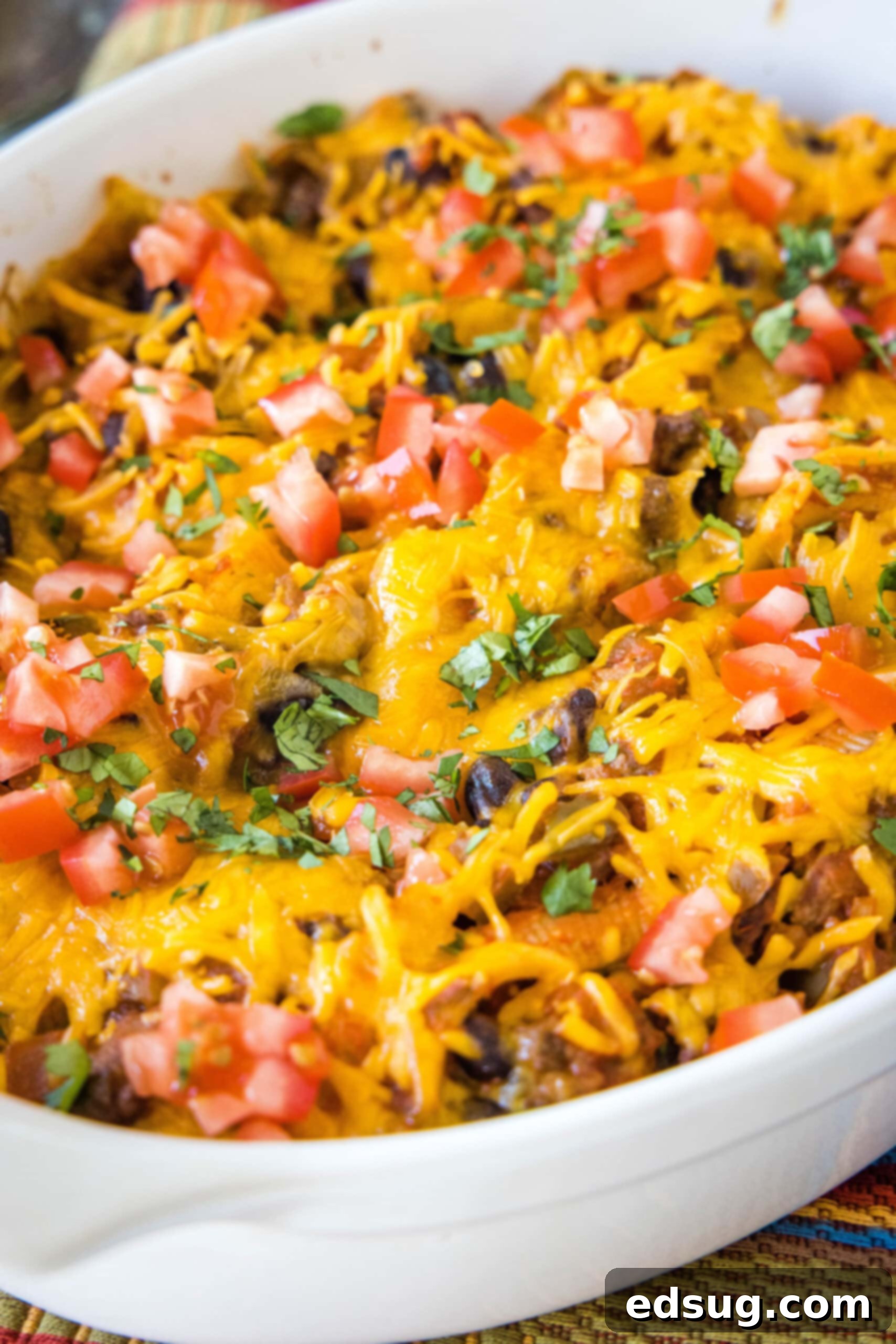 Baked taco stuffed shells in a baking dish, garnished with fresh diced tomatoes and vibrant cilantro, highlighting the finished dish.