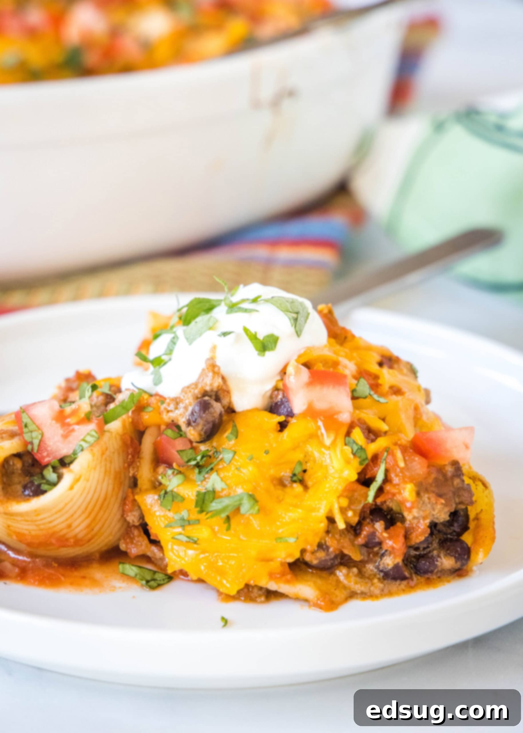 A serving of taco stuffed shells on a white plate next to a fork, ready to be eaten, showing the perfectly baked, cheesy dish.