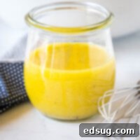 A jar of apple cider vinaigrette on a countertop next to a whisk.