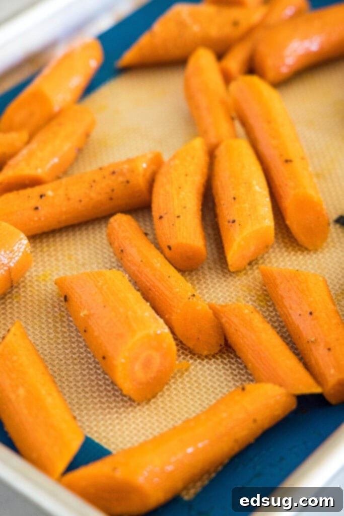 Seasoned carrots spread in a single layer on a baking sheet, ready to roast.