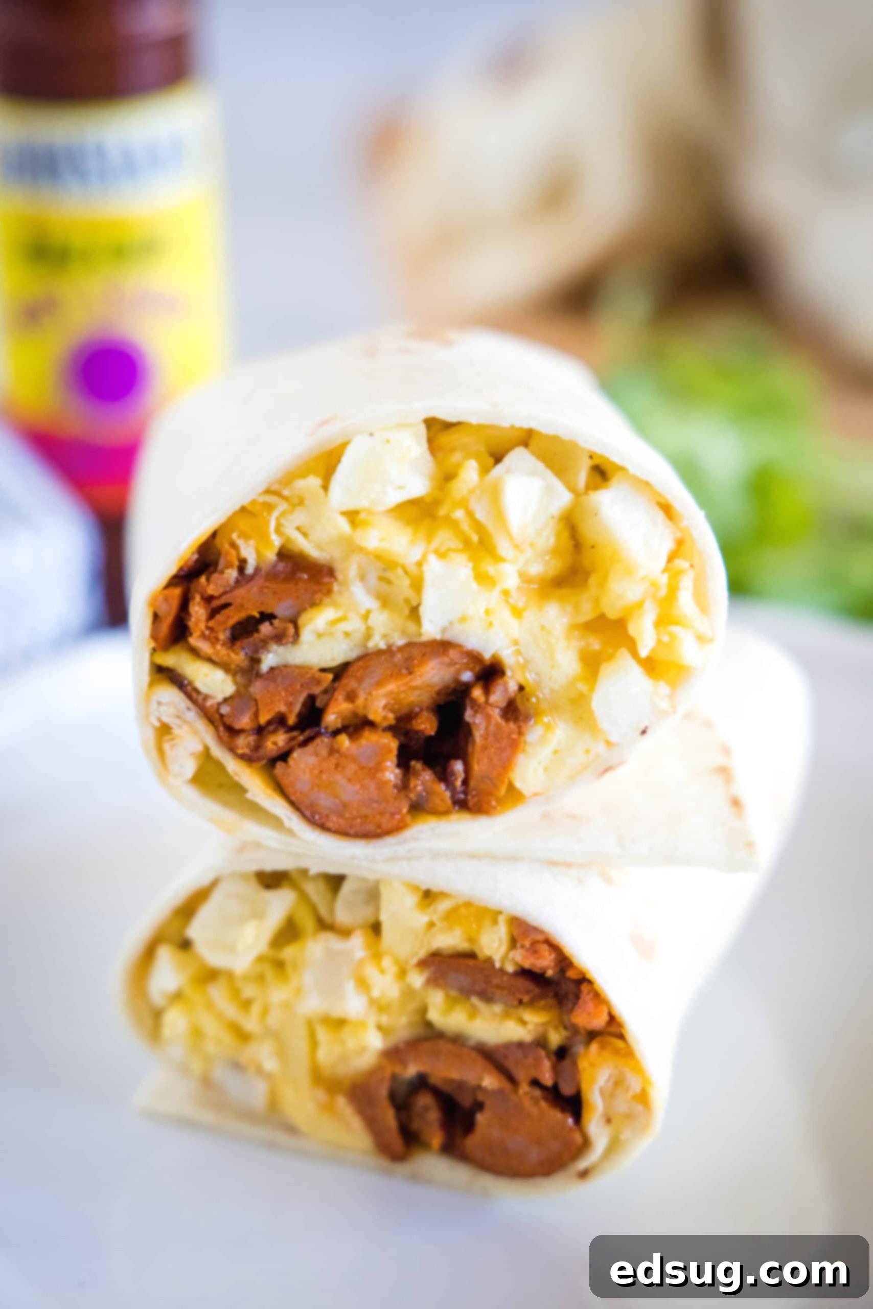 Two halves of a chorizo breakfast burrito stacked on a plate, showing the eggs, cheese, potatoes, and chorizo filling inside.
