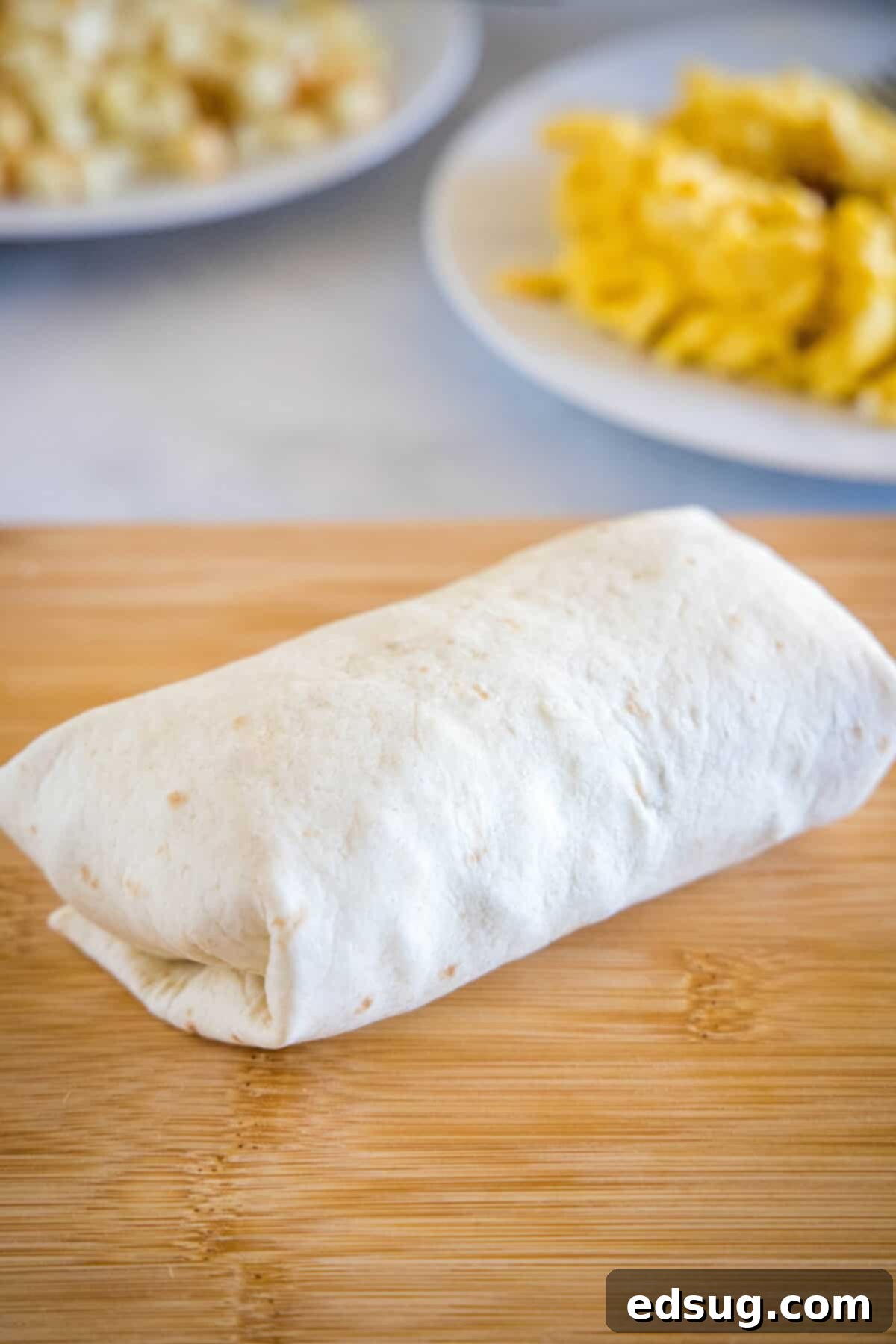 A rolled up breakfast burrito on a wooden cutting board.