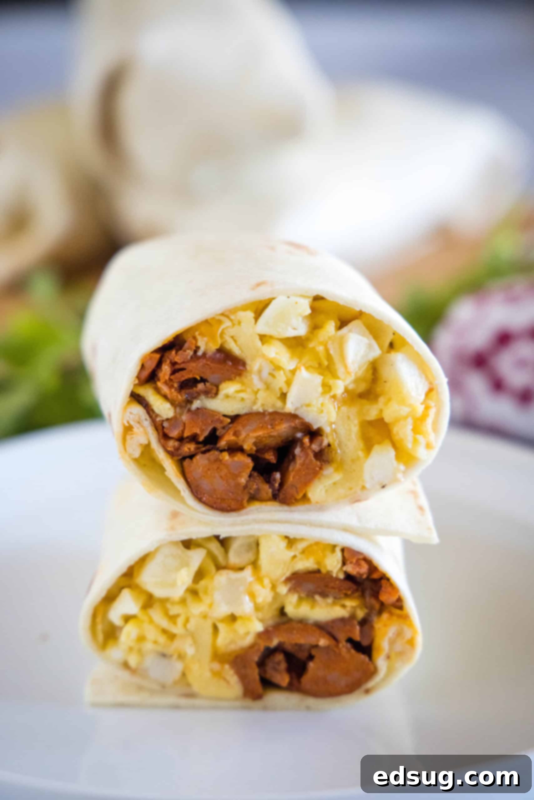 Two halves of a chorizo breakfast burrito stacked on a plate, showing the eggs, cheese, potatoes, and chorizo filling inside.