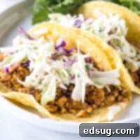 Two tofu tacos topped with Mexican coleslaw and avocado cream on a white plate.
