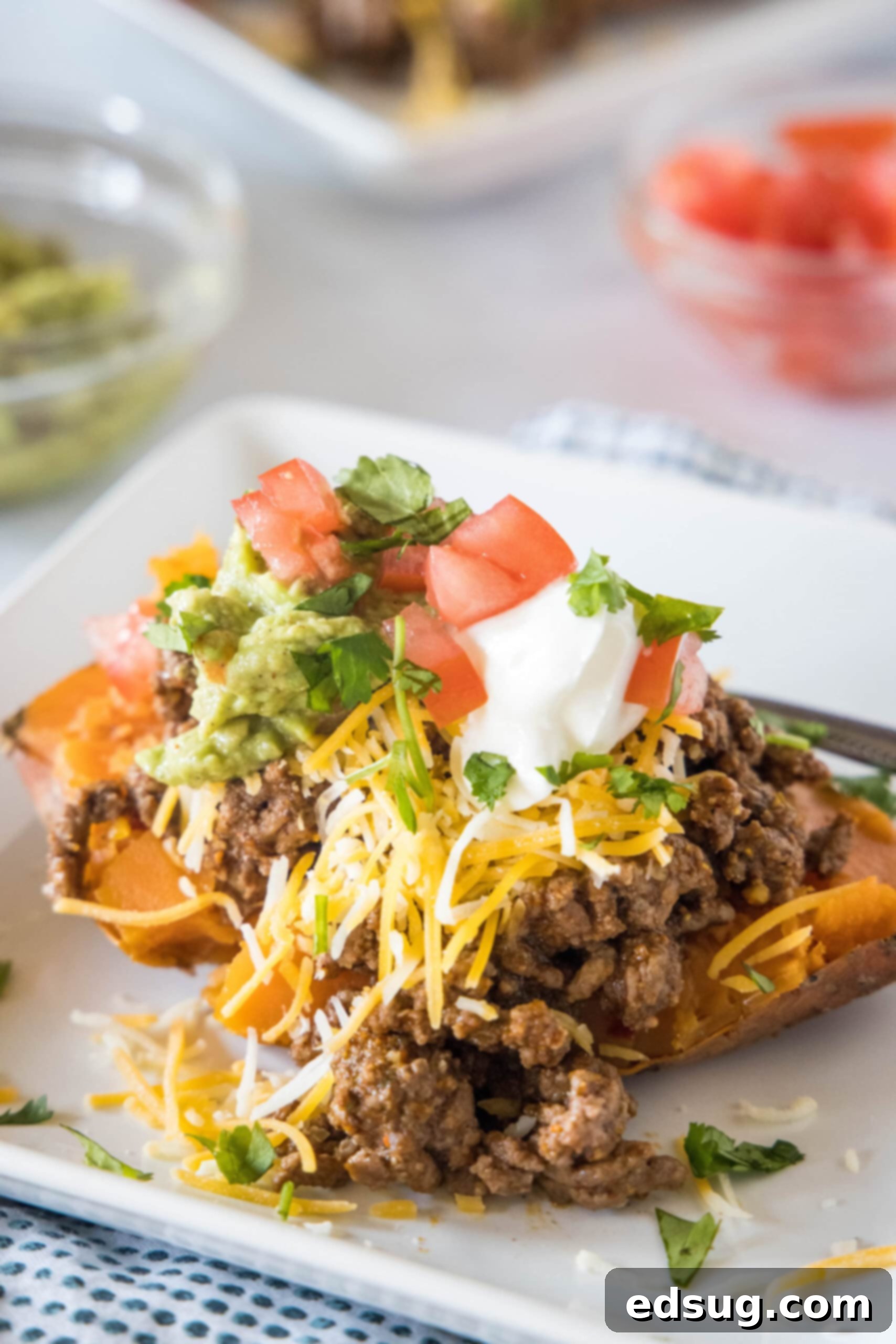 A taco sweet potato piled with taco toppings served on a white plate, with bowls of toppings in the background.