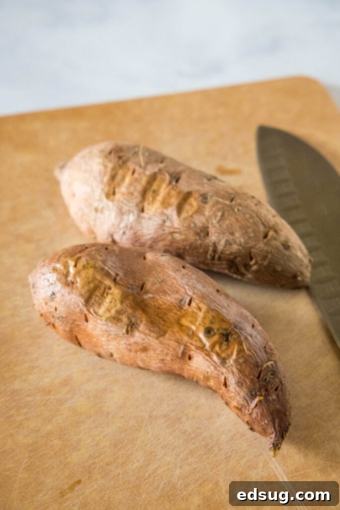 Two sweet potatoes on a wooden cutting board next to a large knife.