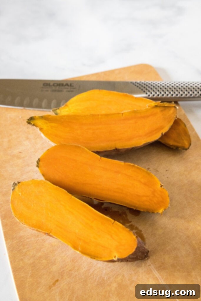 Sweet potatoes cut in half on a wooden cutting board, with a knife in the background.