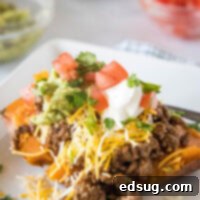 A taco sweet potato piled with taco toppings served on a white plate, with bowls of toppings in the background.