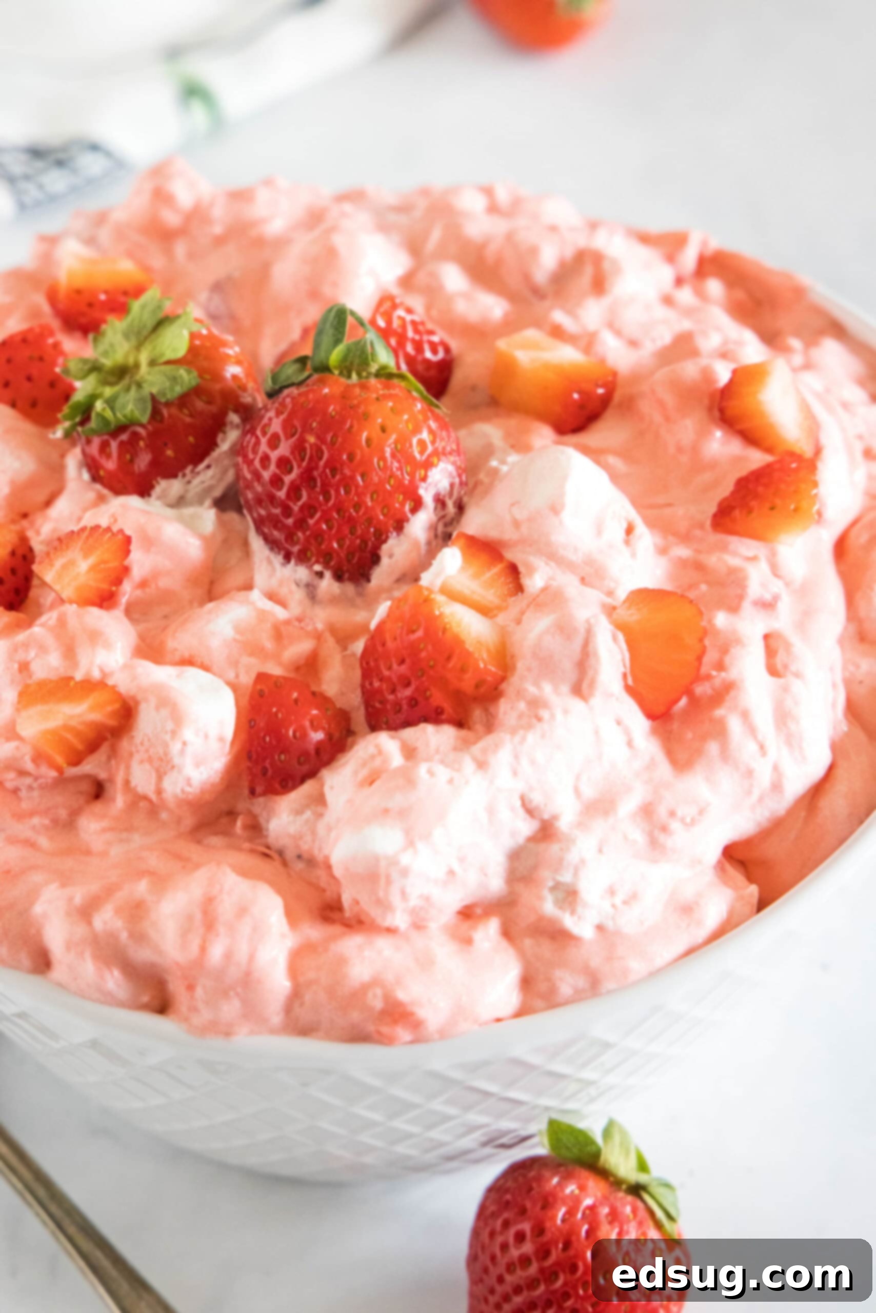 Strawberry fluff topped with chopped strawberries in a white bowl. A perfect light and creamy dessert salad for summer.