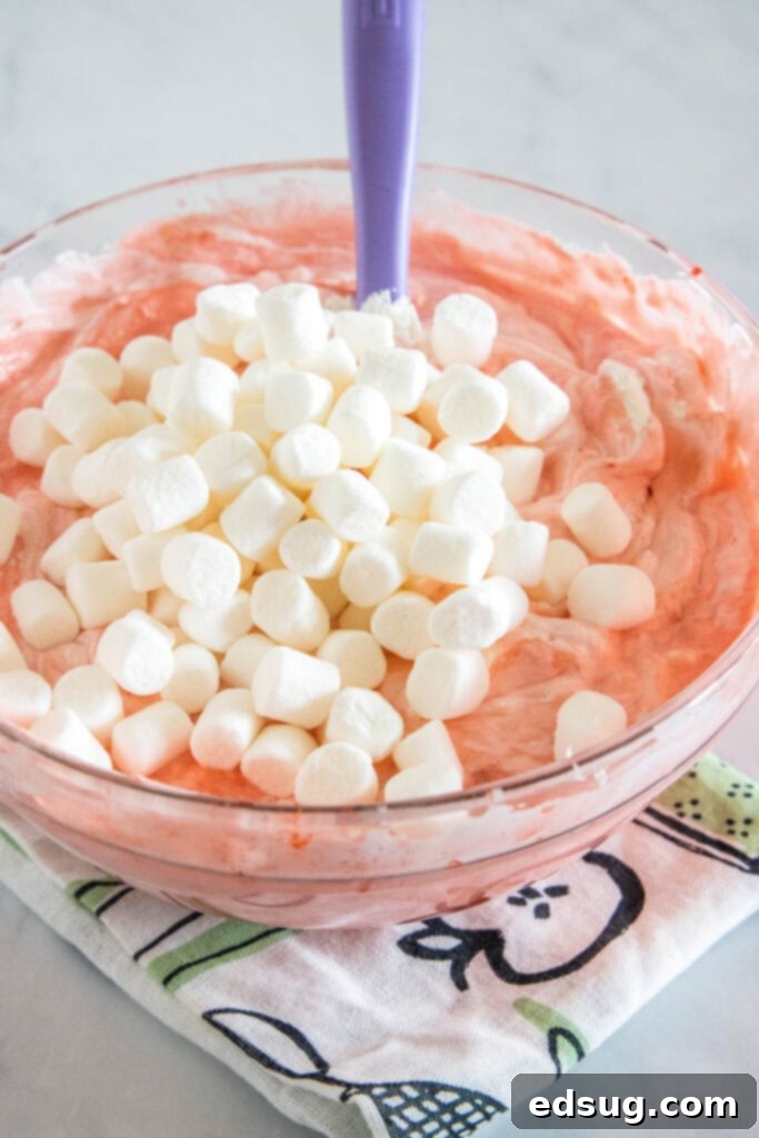 Mini marshmallows added to a bowl of strawberry fluff ingredients, ready to be gently folded in.