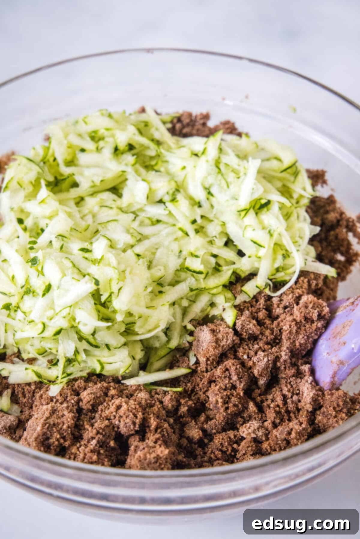 Adding shredded zucchini to brownie batter in a bowl