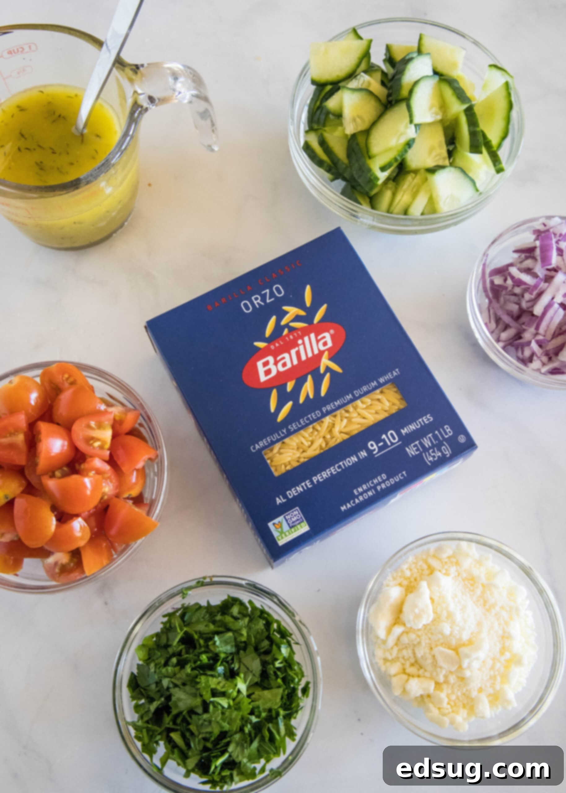 Ingredients for orzo pasta salad laid out on a white surface.