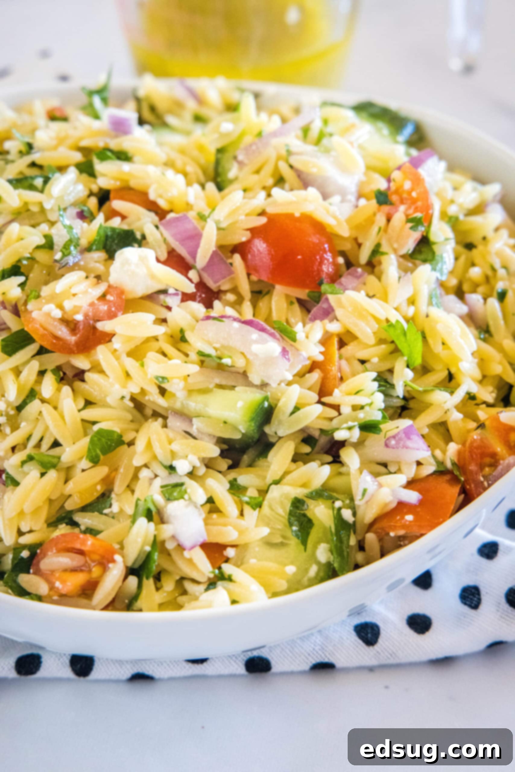 Orzo pasta salad in a large bowl resting on top of a black and white polka dot dishcloth, highlighting the texture and colors.