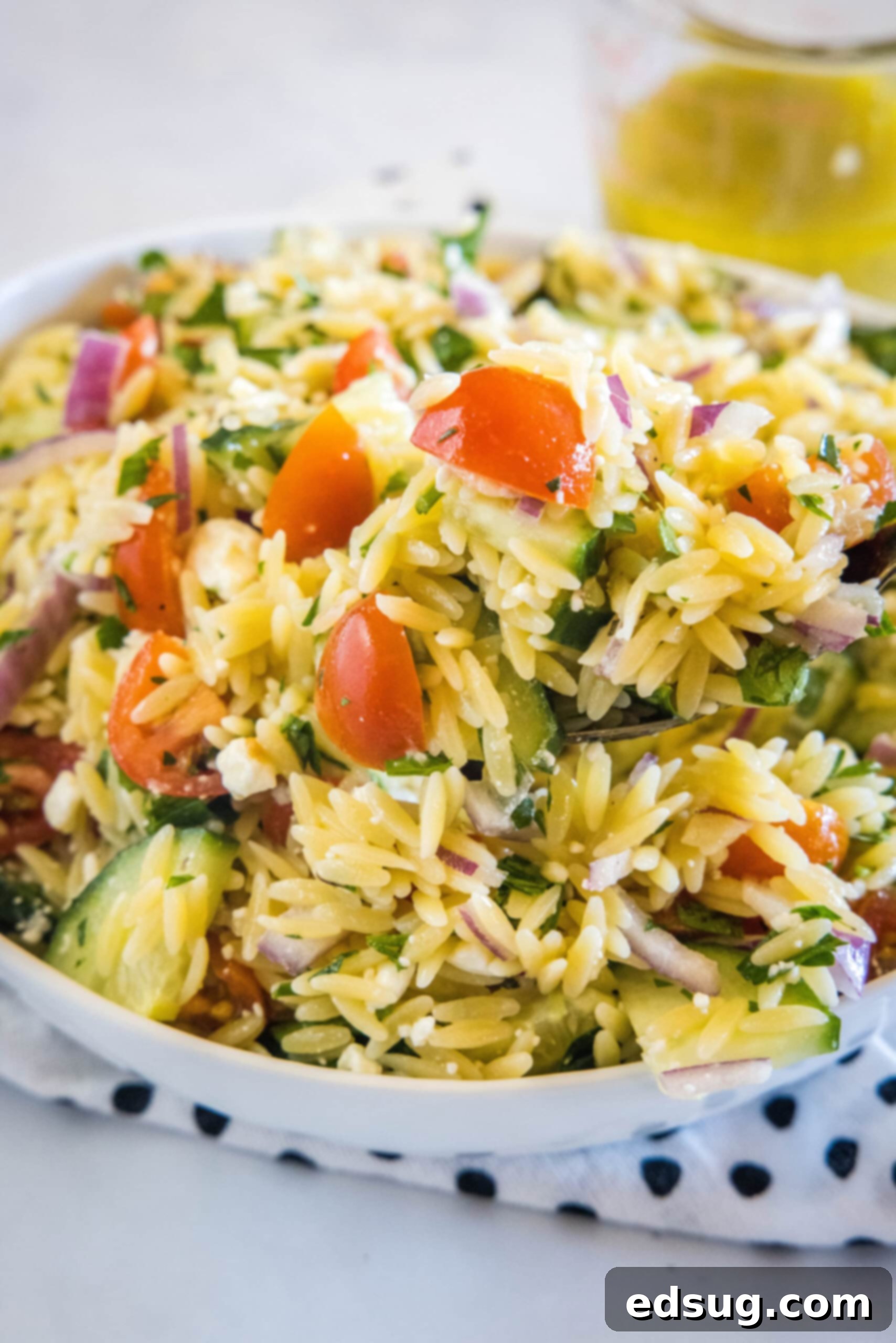 Orzo pasta salad in a large bowl resting on top of a black and white polka dot dishcloth, offering a different angle of the finished dish.