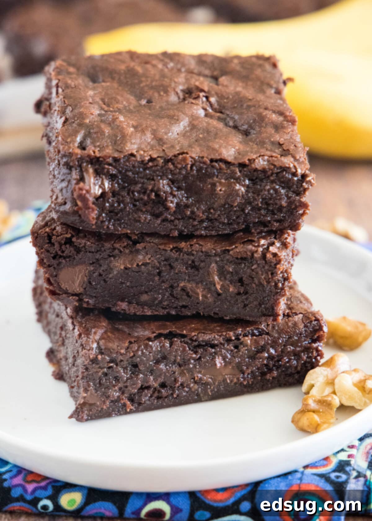 stacked fudgy banana brownies on a white plate with glossy, crackly tops