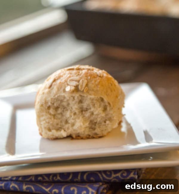 A close-up of a single buttermilk oat roll on a plate, cut in half to show its soft, fluffy interior, alongside a pat of melting butter.
