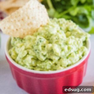 cropped close up roasted garlic guacamole in a bowl with a tortilla chip