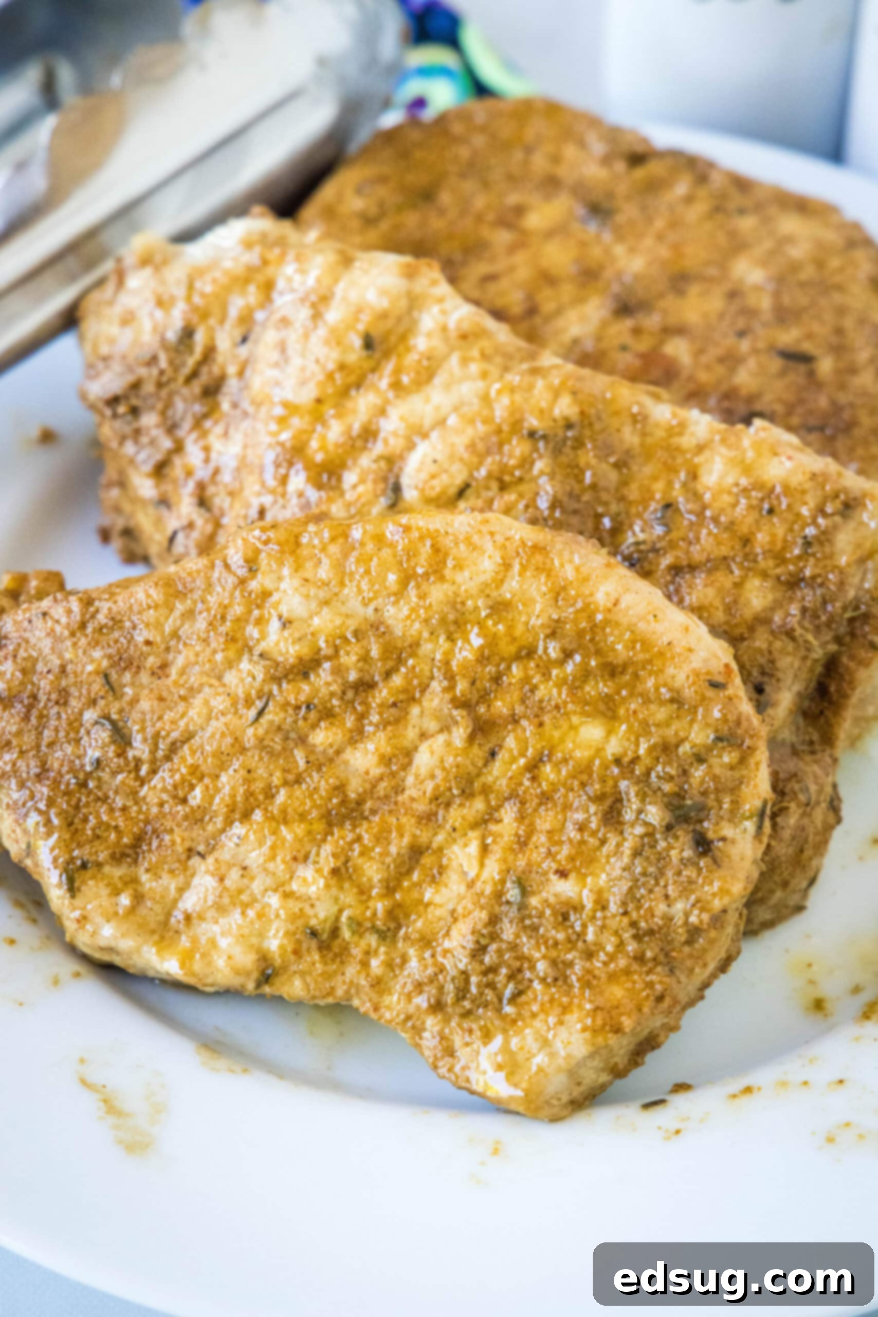 Cooked seasoned pork chops on a white plate next to a set of tongs, ready to be served.