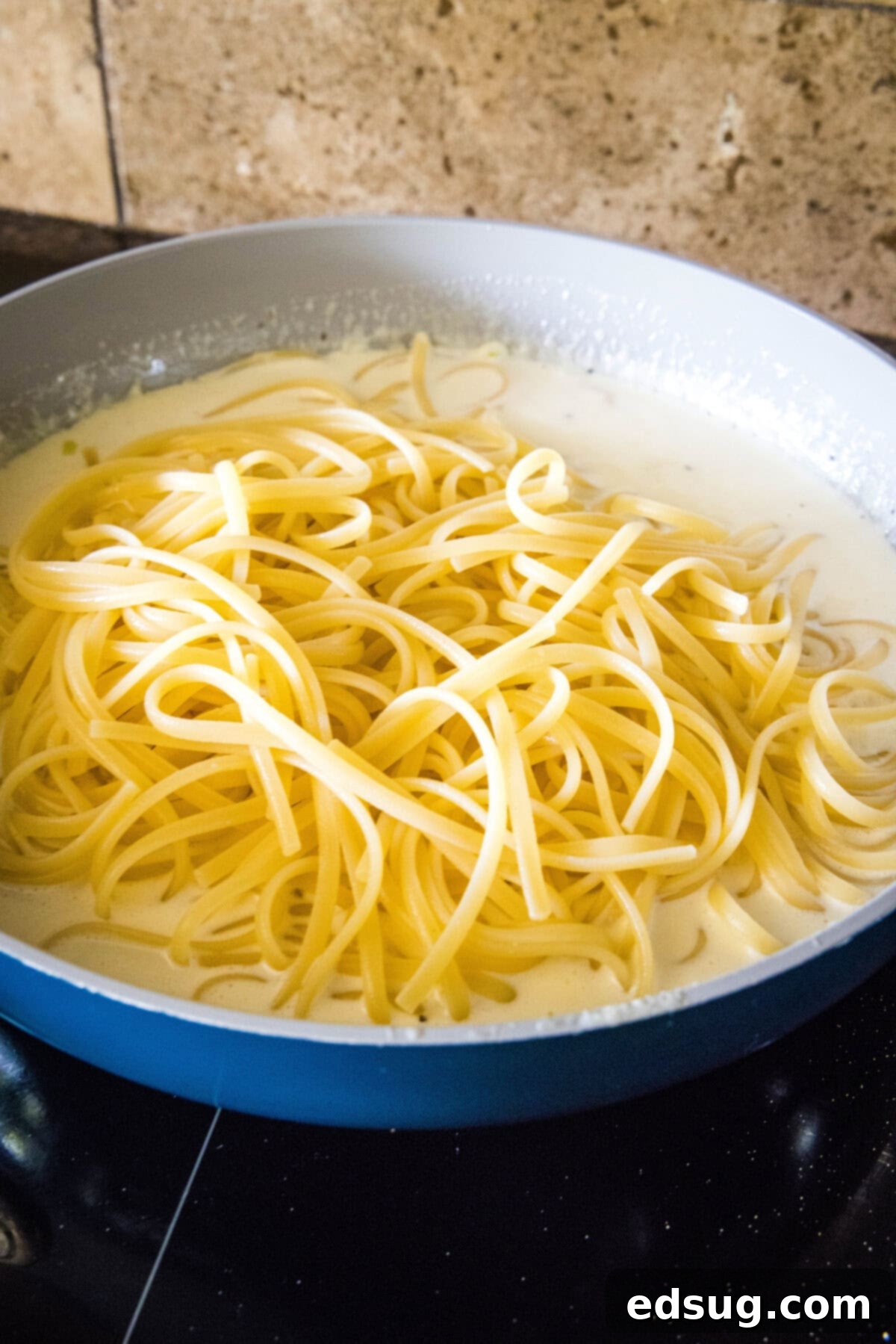 This easy homemade Alfredo sauce is rich and creamy and packed with garlicky parmesan flavors. Make it in one pan with your favorite pasta! Fettuccine pasta added to homemade alfredo sauce in a skillet.