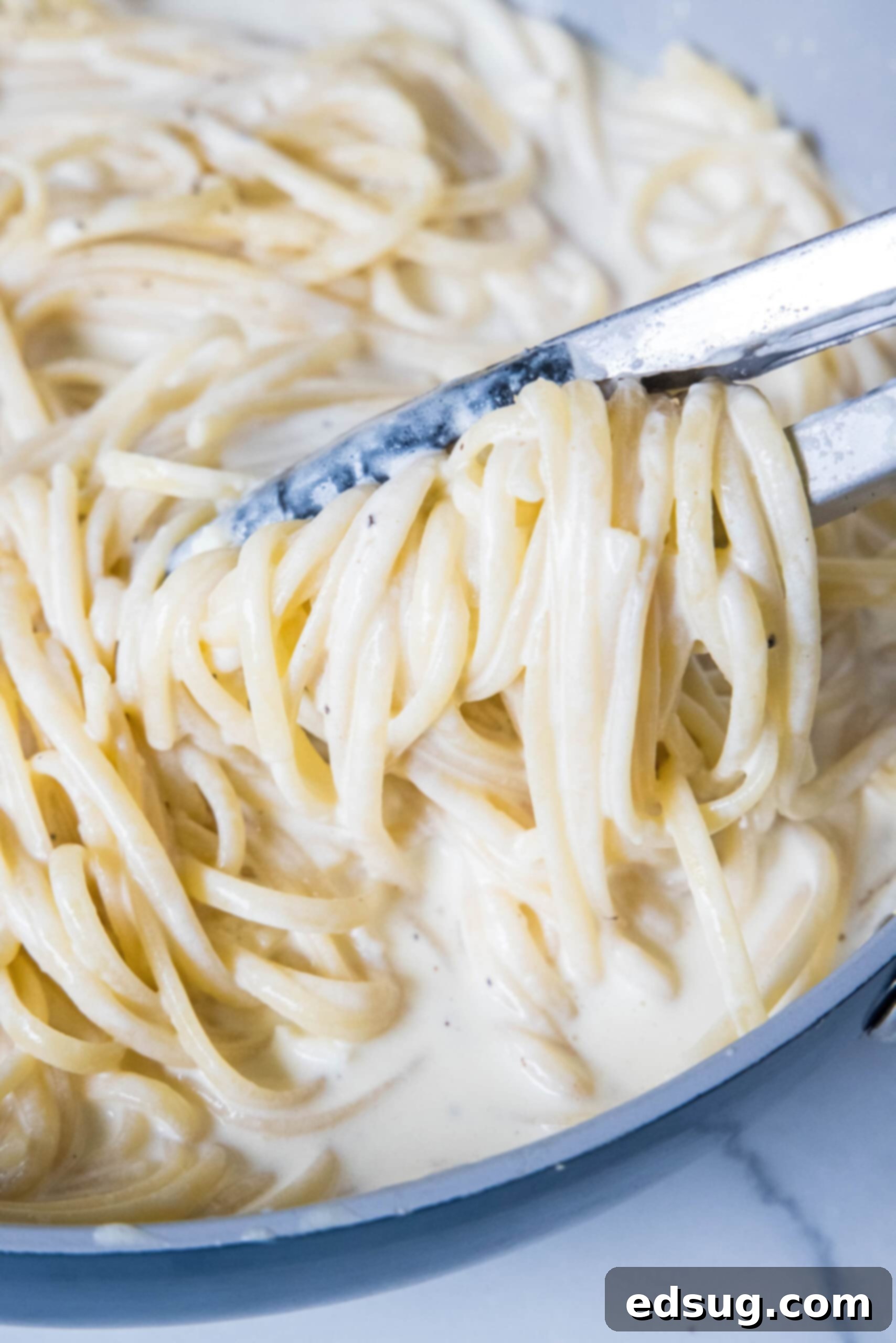 This easy homemade Alfredo sauce is rich and creamy and packed with garlicky parmesan flavors. Make it in one pan with your favorite pasta! Metal tongs lifting homemade alfredo pasta from a skillet.
