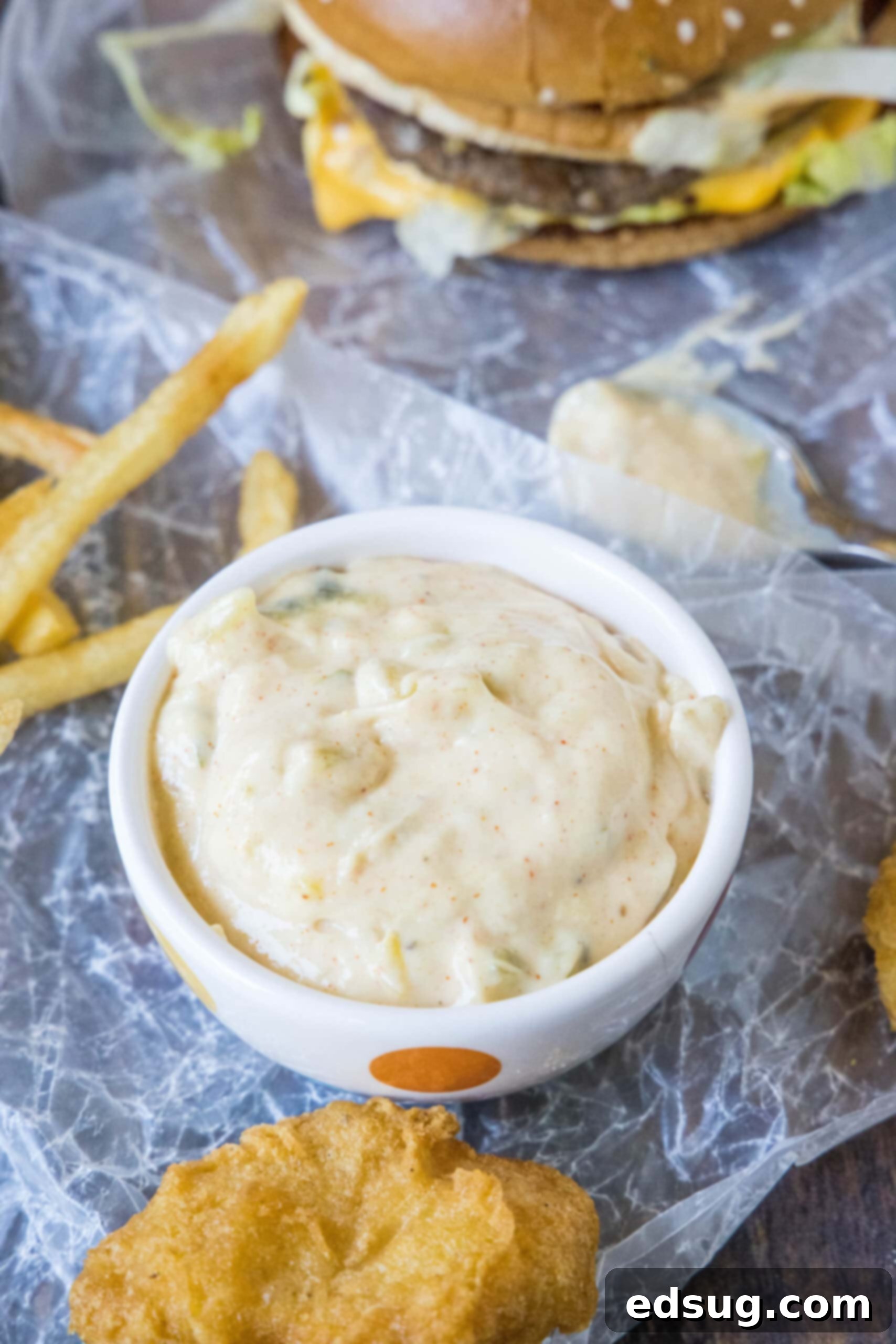 Homemade Big Mac Sauce in a small serving bowl, with a juicy burger and golden fries blurred in the background, ready for dipping.
