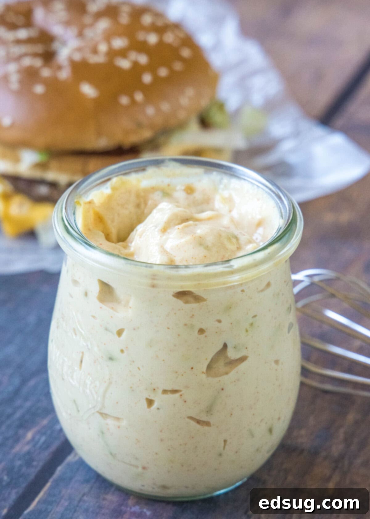 Homemade Big Mac Sauce stored neatly in a clear glass jar, with a delicious burger blurred in the background, ready for a flavorful meal.
