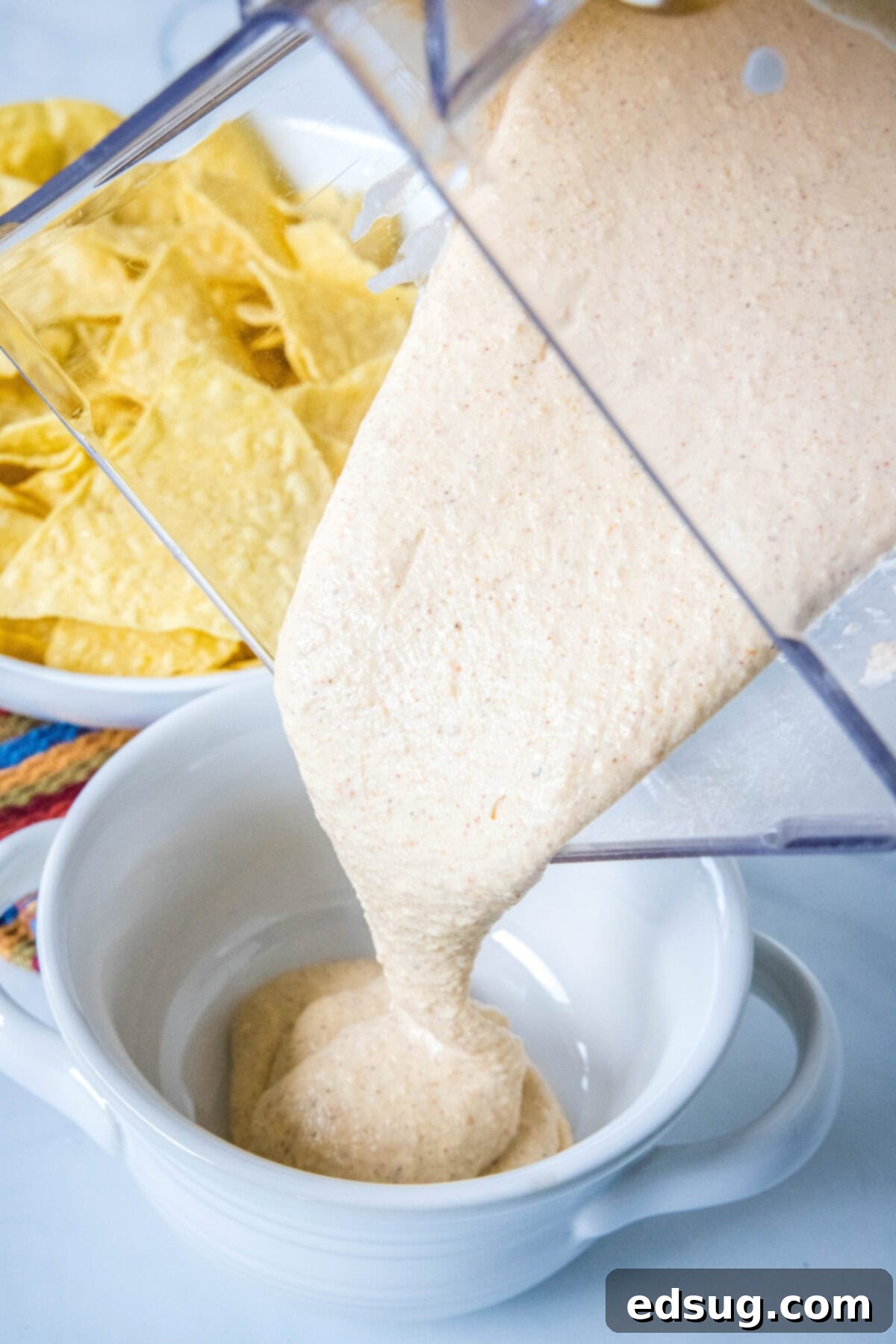 smooth cottage cheese queso being poured from a blender into a white serving bowl