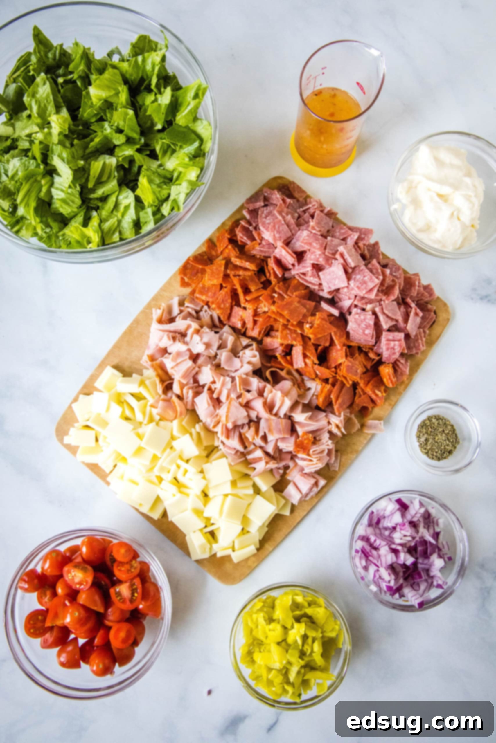 A colorful array of fresh and savory ingredients neatly arranged for making hoagie dip, including deli meats, cheese, tomatoes, and lettuce.
