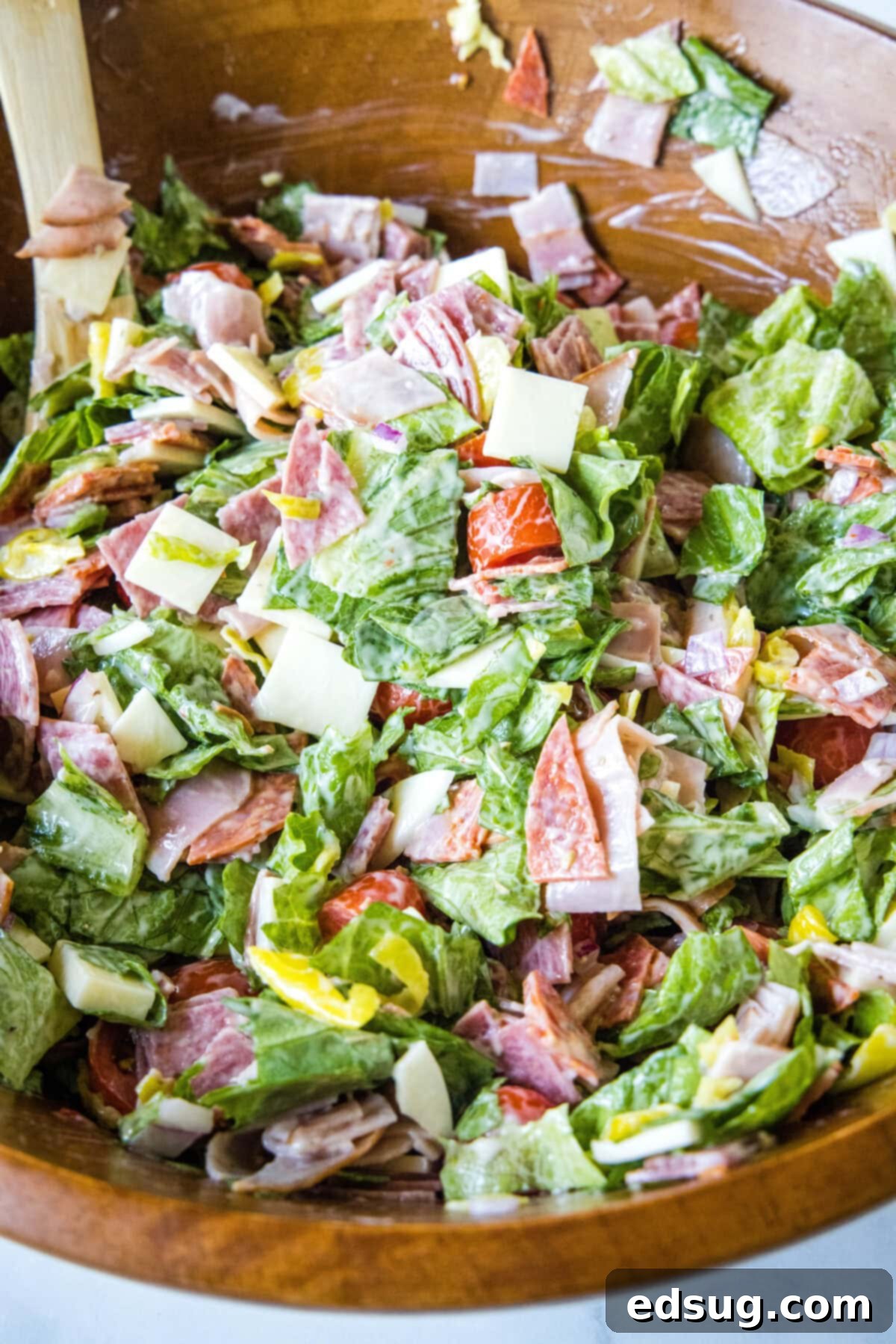 Close-up of freshly tossed hoagie dip in a wooden bowl, showing the vibrant mix of ingredients and creamy dressing, ready to serve with a spoon.