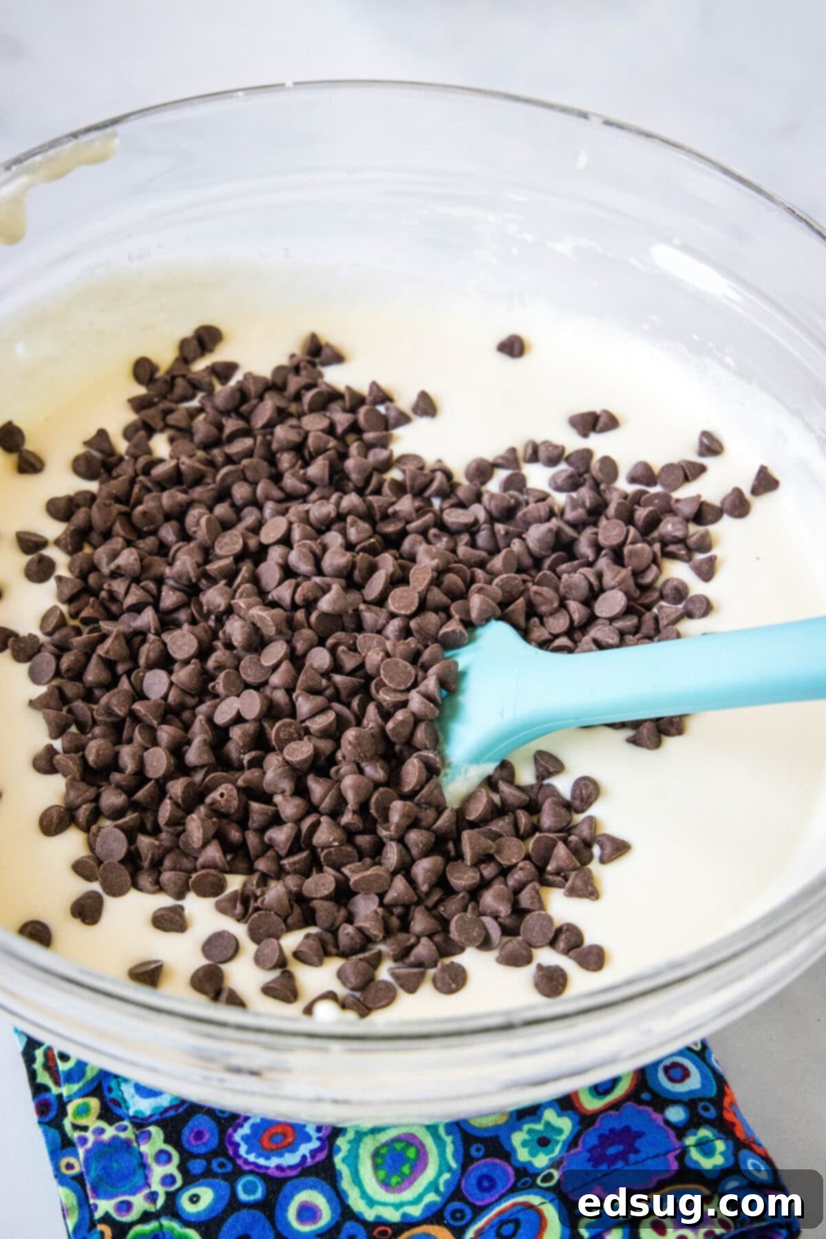 Mini chocolate chips being gently folded into the smooth, prepared cannoli dip mixture in a glass bowl, creating a delightful texture.