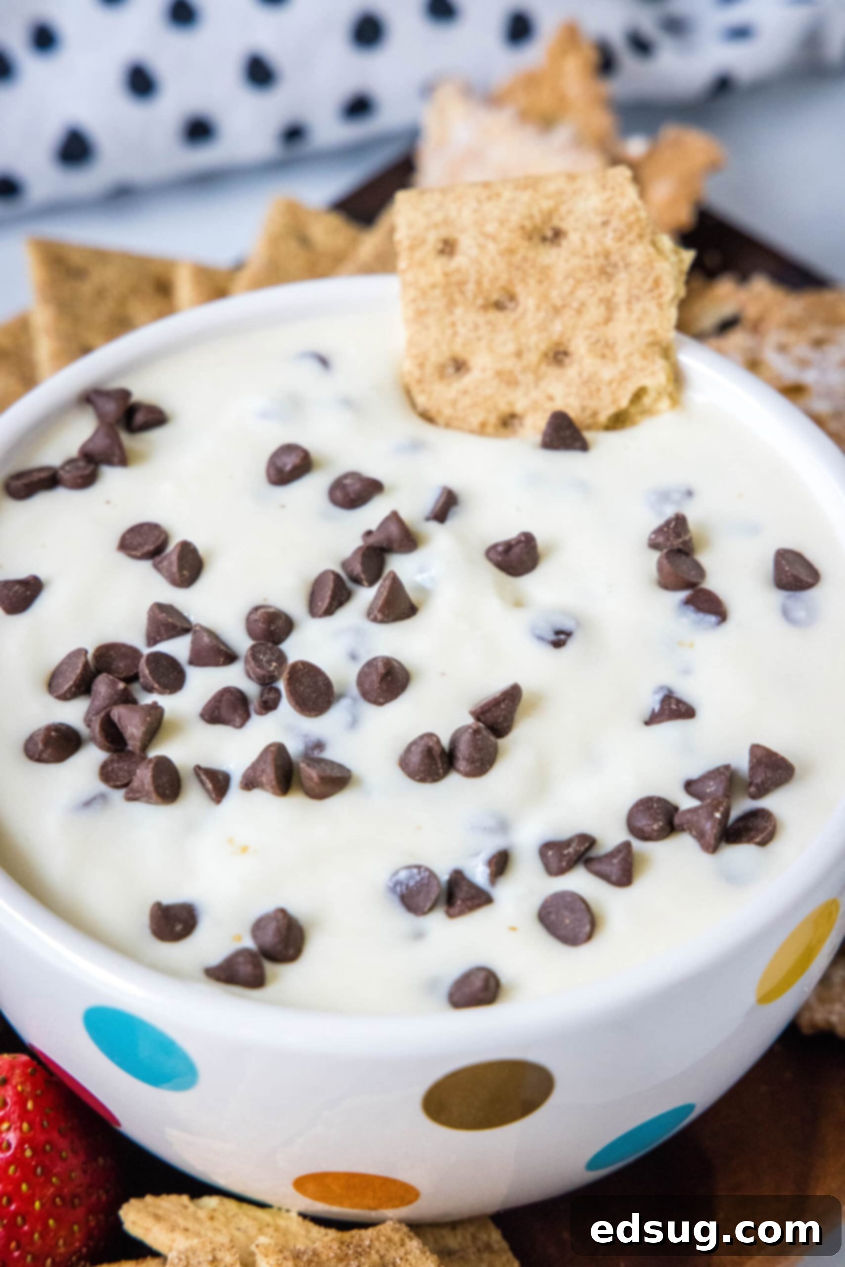Close-up shot of creamy cannoli dip in a small white bowl, with a single graham cracker perfectly positioned, ready to scoop, showcasing the mini chocolate chips.
