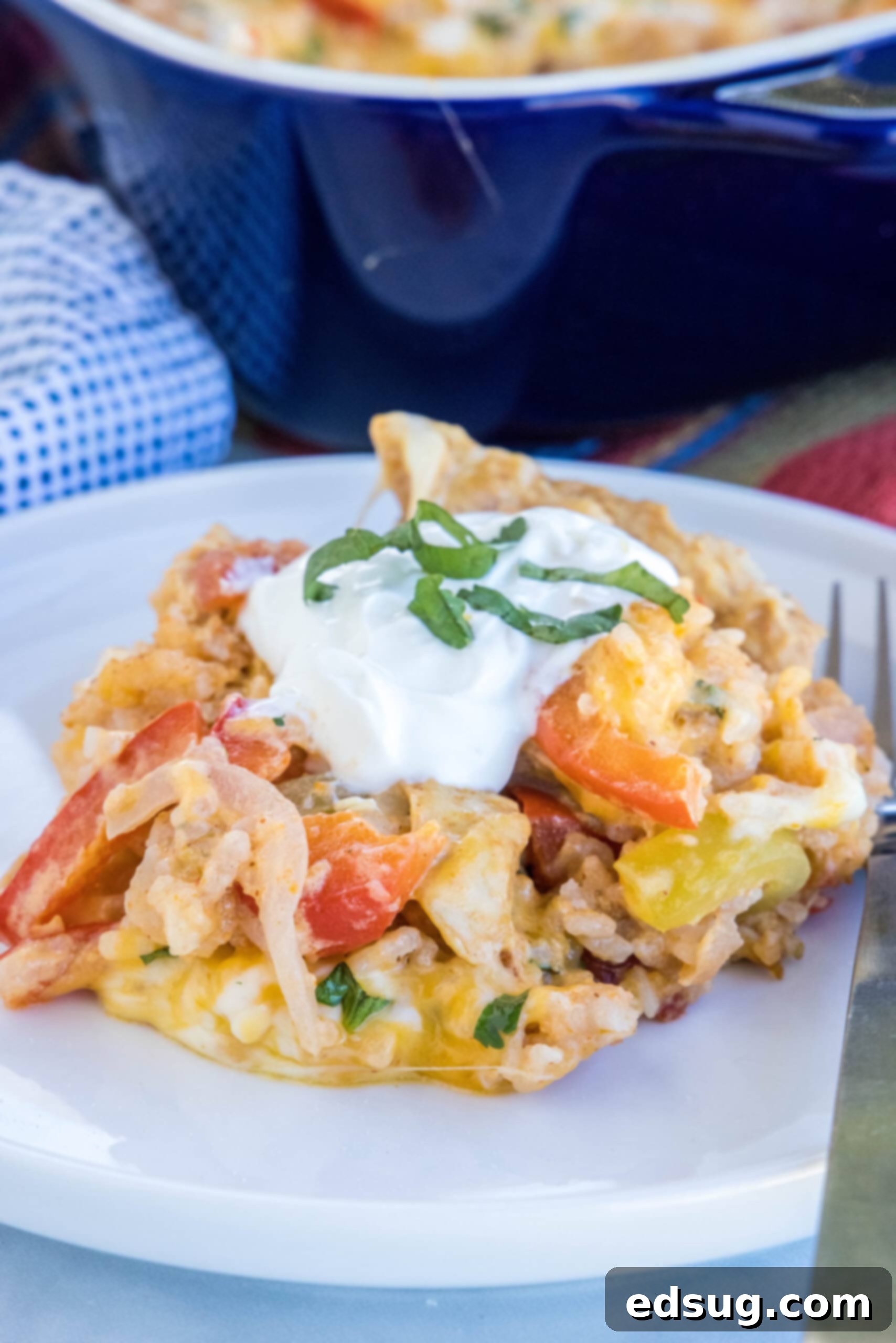 A single serving of chicken fajita casserole on a white plate next to a fork, ready to be eaten.
