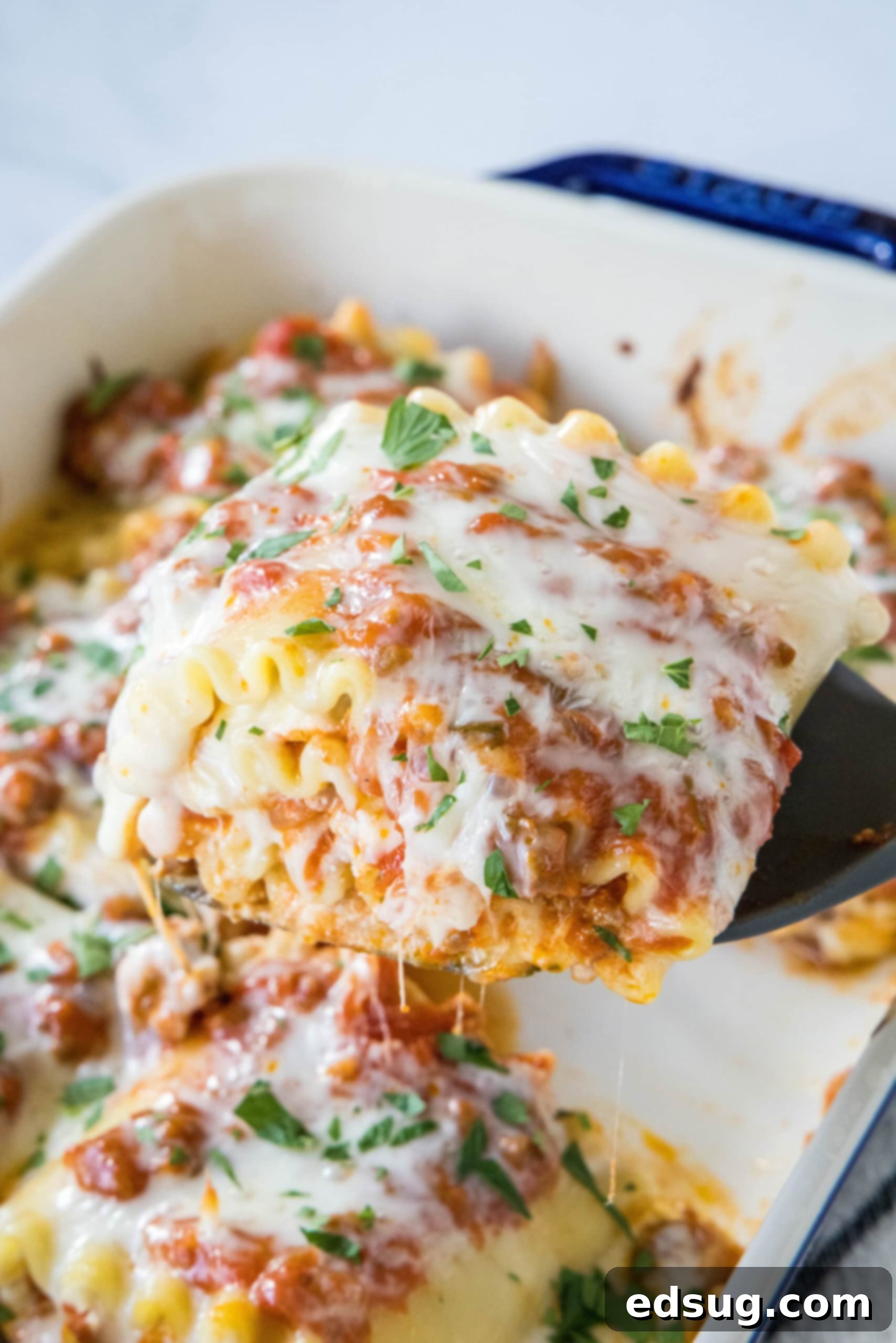A spatula lifting a lasagna roll up from a baking dish.