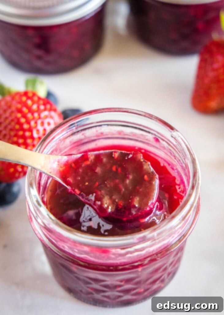 Berry Medley Jam 2 Spoonful of vibrant mixed berry jam being scooped from a glass jar, showcasing its rich texture and fruit chunks.