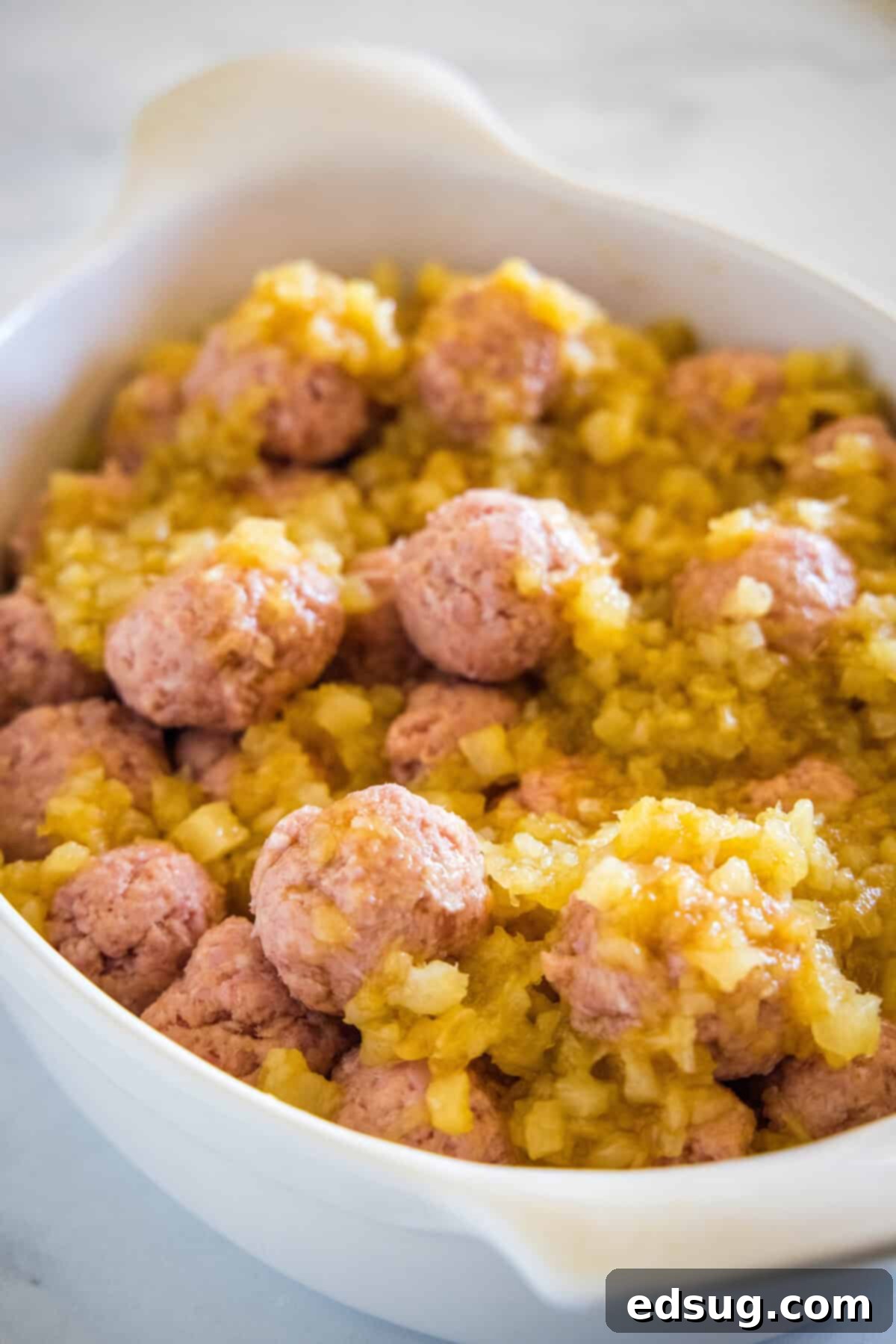 Unbaked ham balls generously covered with sweet pineapple sauce in a ceramic baking dish, ready for the oven.